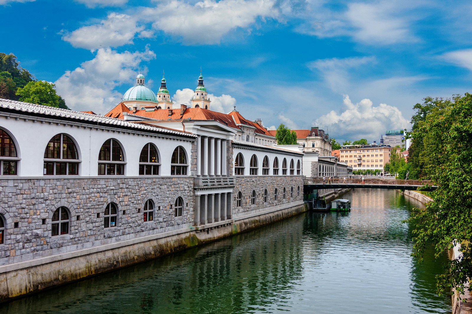 Lubiana, Slovenia: guida city break tra Castello, Ljubljanica e Ponti di Plečnik 3 I colonnati bianchi del Mercato Centrale di Plečnik lungo la Ljubljanica a Lubiana con le cupole verdi della Cattedrale di San Nicola sullo sfondo