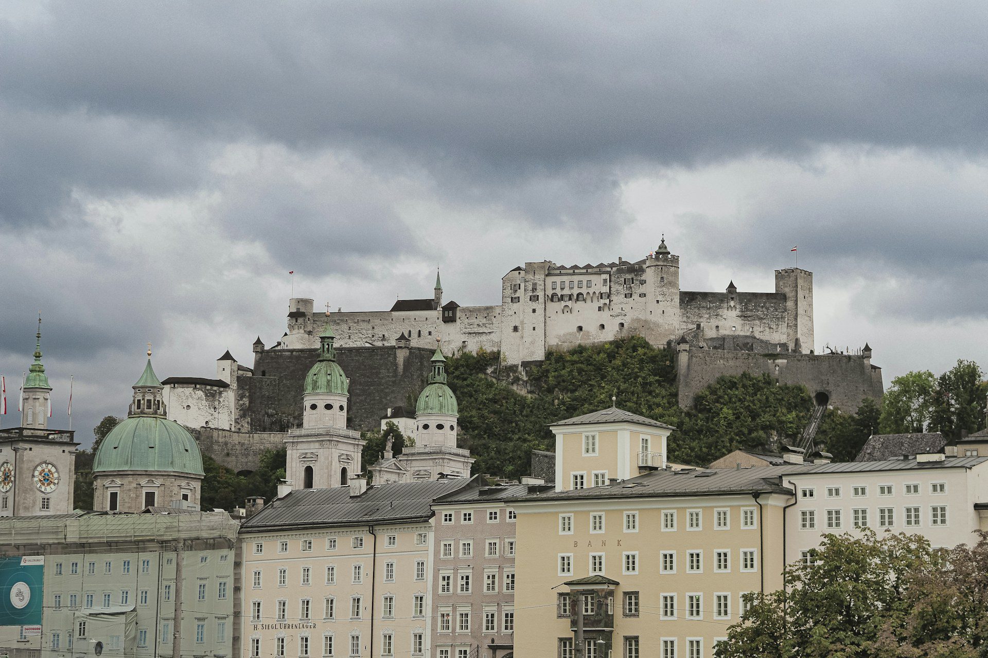 Salisburgo, Austria: guida city break tra Mozart, Fortezza e Città Vecchia 3 Le cupole verdi e i campanili barocchi del centro storico di Salisburgo sotto la Fortezza di Hohensalzburg vista dalla riva della Salzach in una giornata nuvolosa