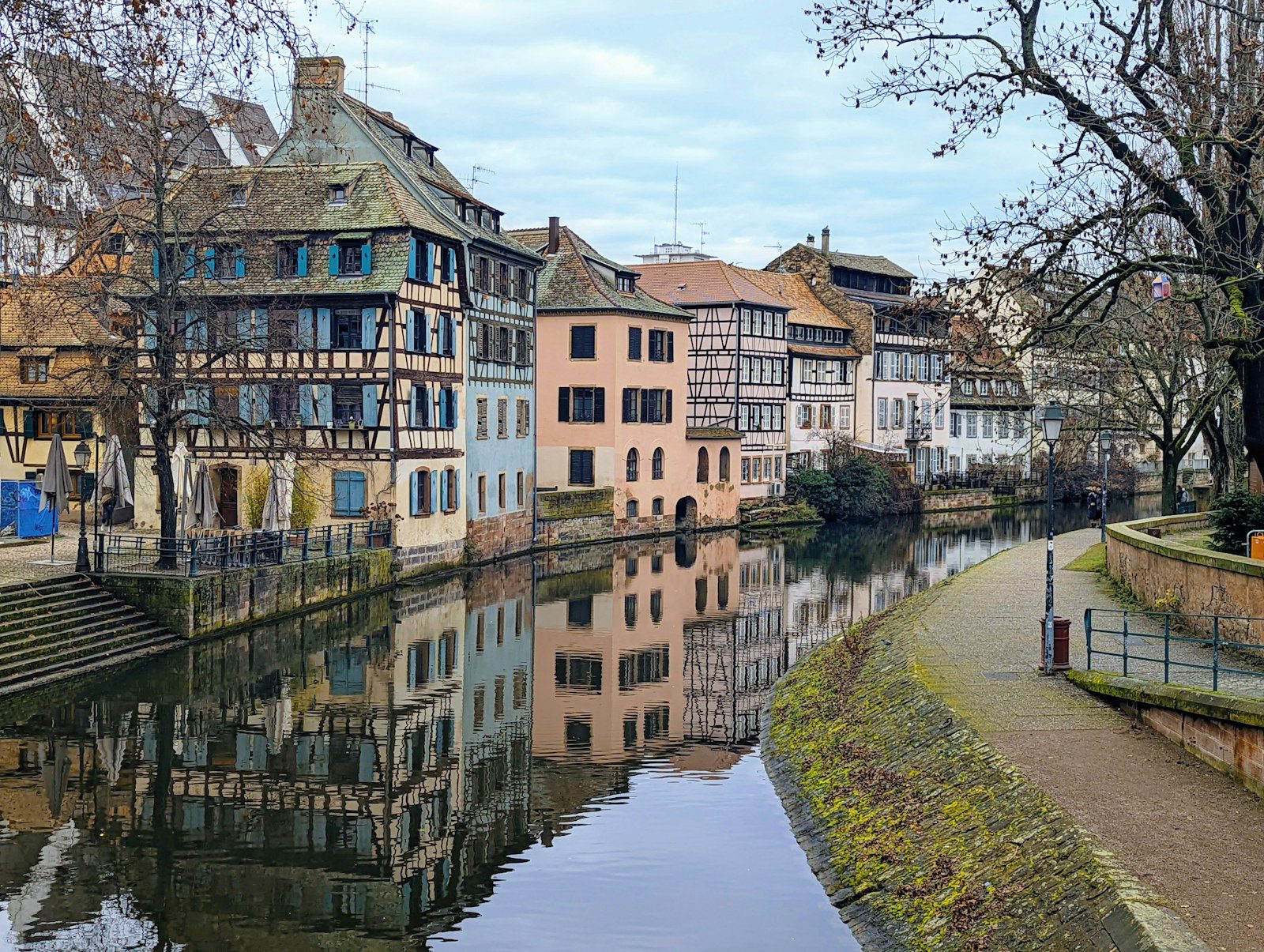 Strasburgo, Francia: guida city break tra Cattedrale, Petite France e mercatini di Natale 3 Case a graticcio della Petite France di Strasburgo in inverno con gli alberi spogli riflesse nell’acqua immobile del canale lungo la passeggiata