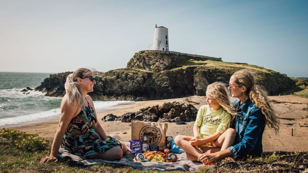 A young family on the beach with a lighthouse in the background, Isle of Anglesey, Wales